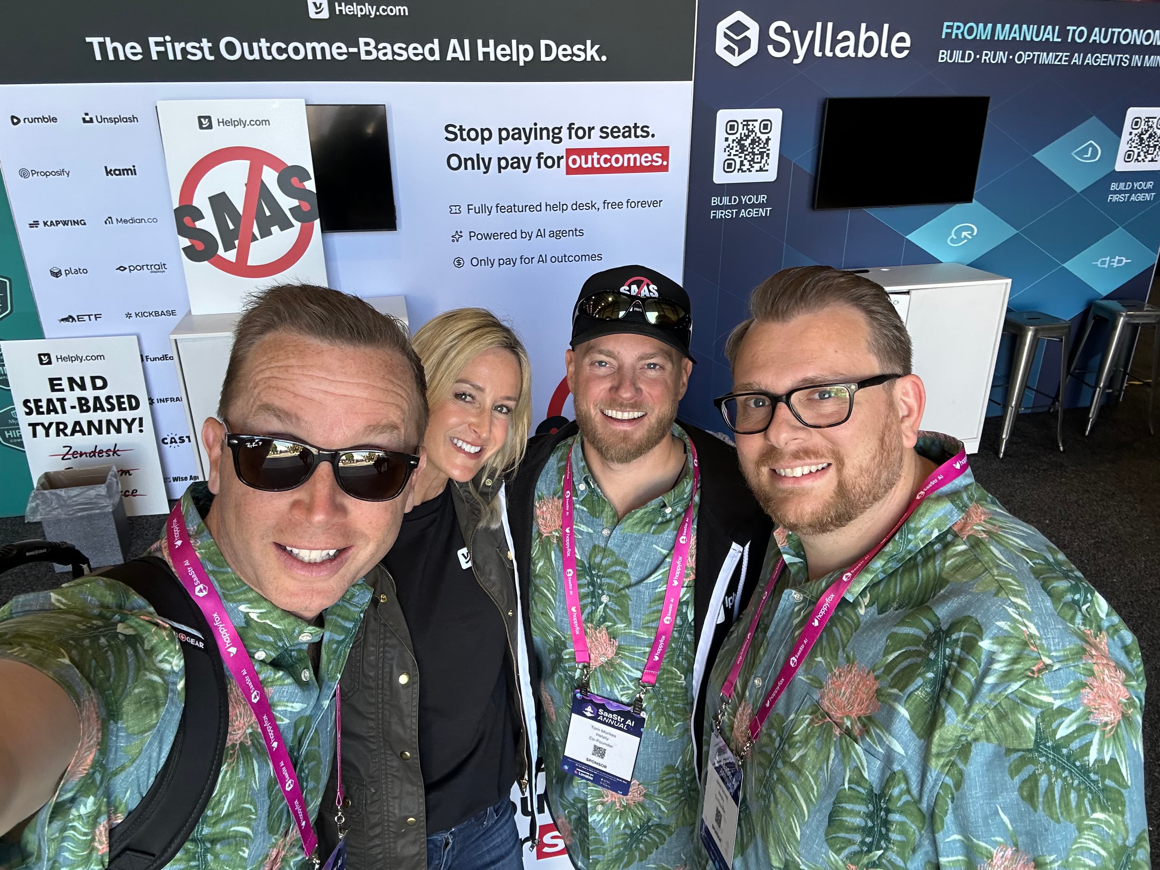 The Helply team at their booth at SaaStr AI Annual, in front of signage for their AI-native help desk
