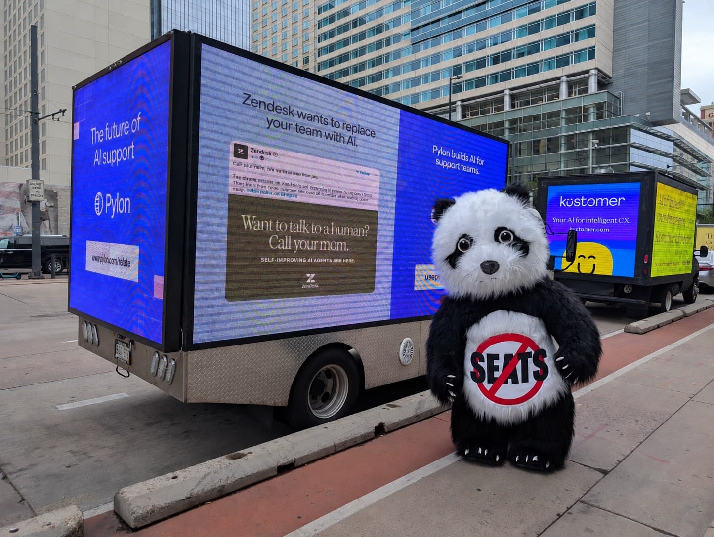 The Helply panda wearing a No Seats sign on the street outside a conference, next to rival ad trucks